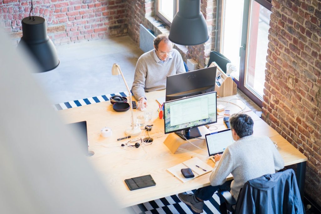 Birds-eye view of a modern office with professionals collaborating on laptops and monitors.
